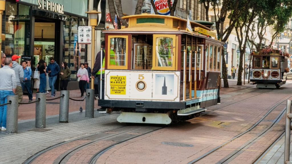 San Francisco cable car traveling through bustling downtown area, showcasing city life.