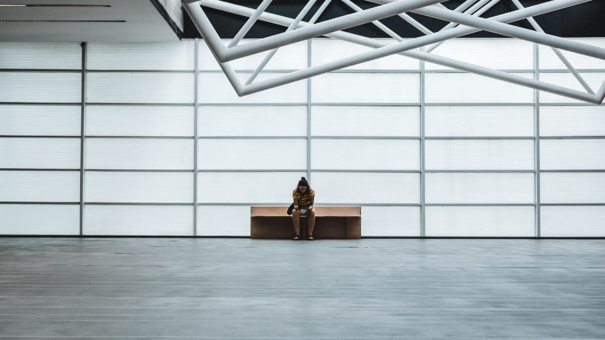 A lone person sits on a bench in a modern, spacious interior with geometric ceiling design.