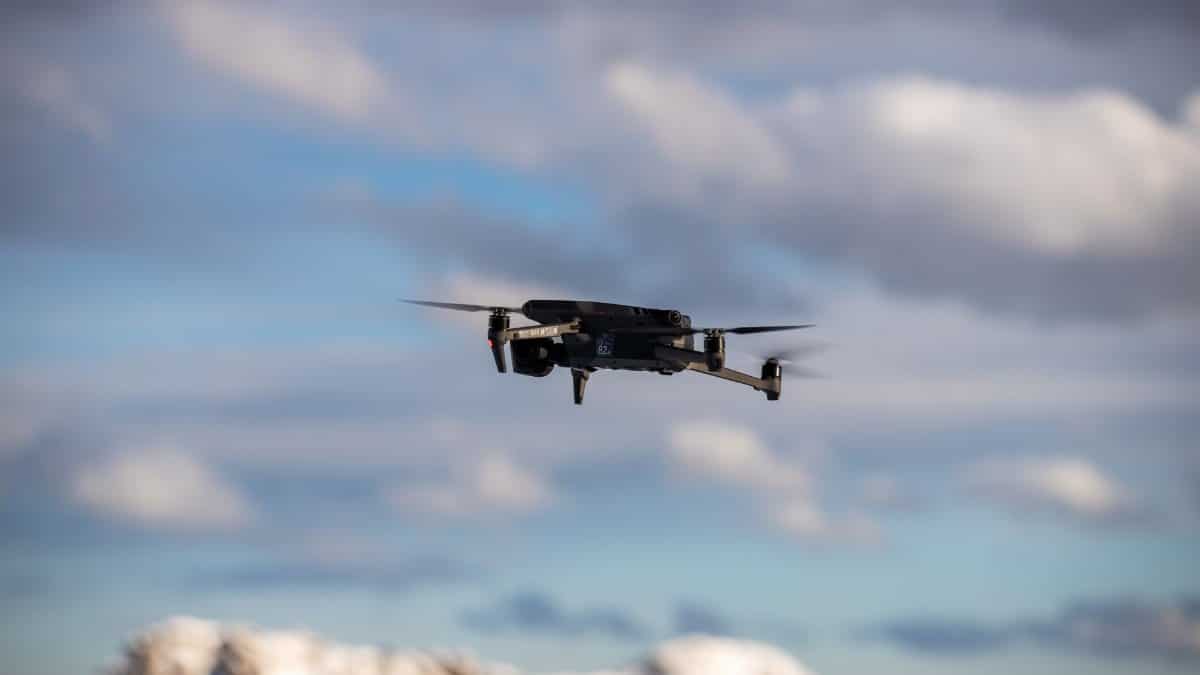 Aerial view of a drone flying over snow-covered mountains with dramatic clouds.