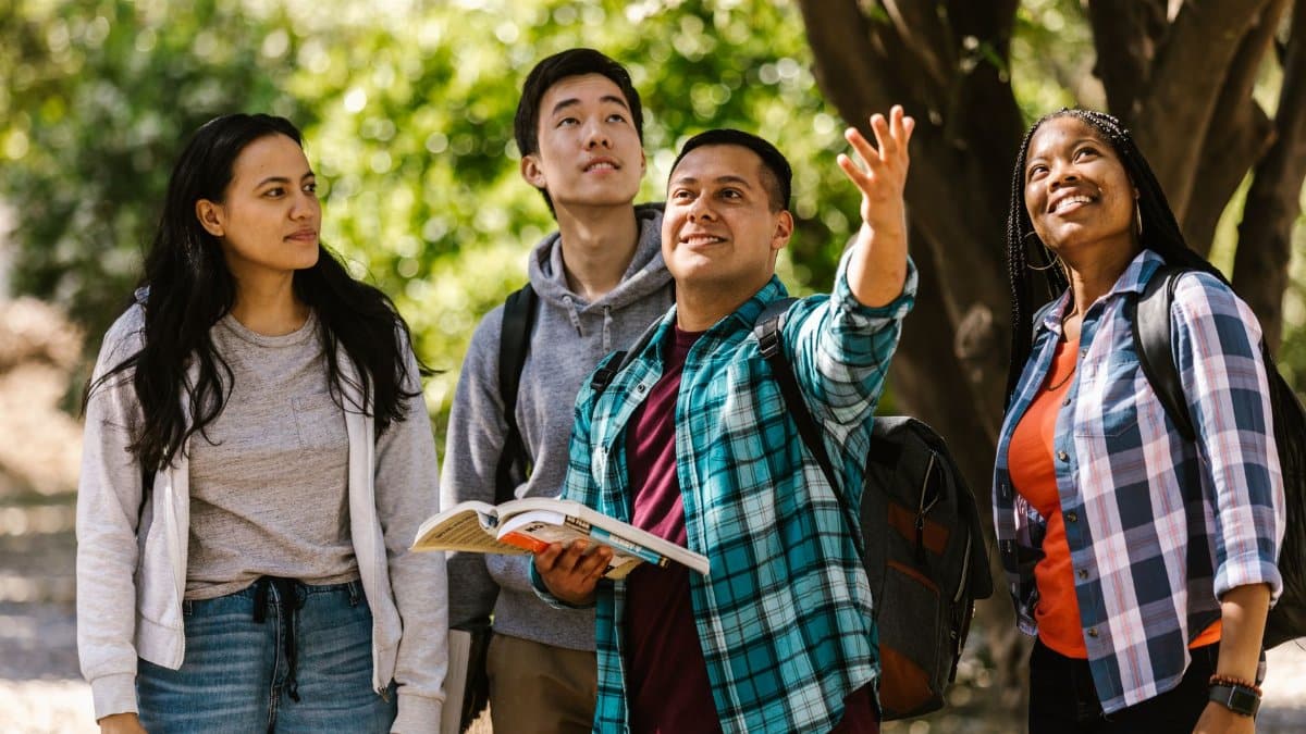 Four diverse college students outdoors, studying and interacting with nature.