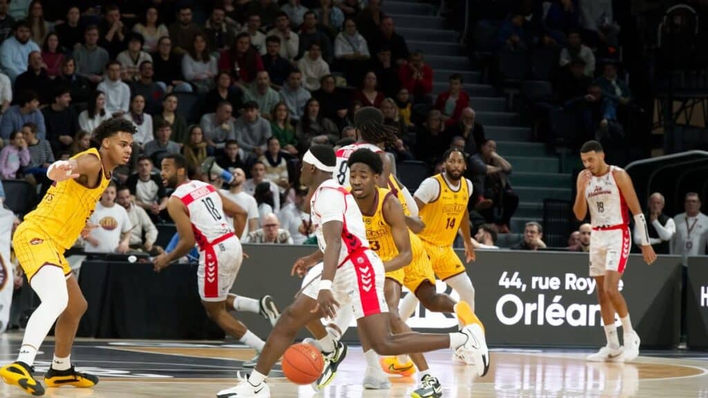 Players in action during an indoor basketball game, with a crowd watching intently.