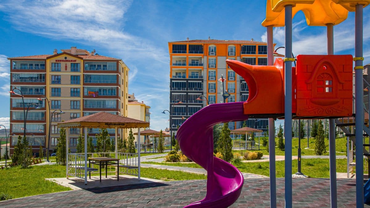 Vibrant playground with a slide in a green urban park amidst modern buildings.