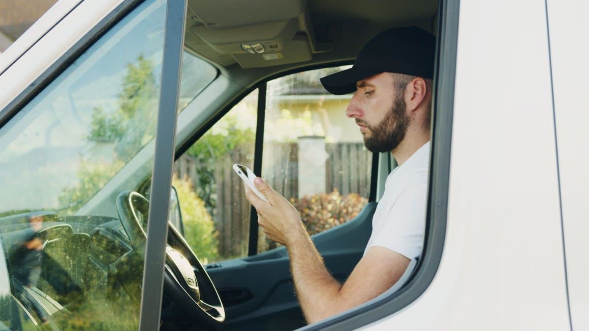 Side view of a man using a smartphone while sitting in a parked vehicle.