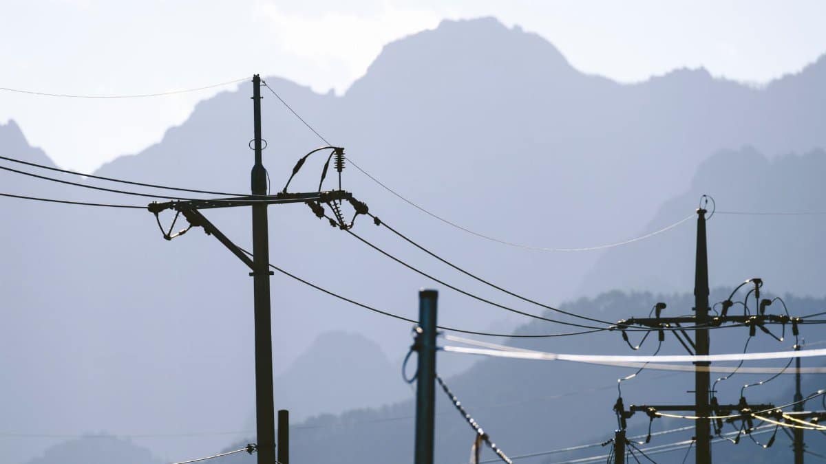 Scenic view of electric poles and wires forming silhouettes against a majestic mountain backdrop.