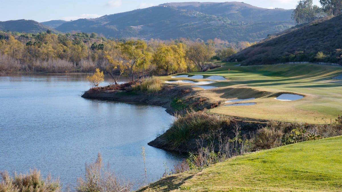 Beautiful landscape view of a golf course by a tranquil lake with distant mountains.