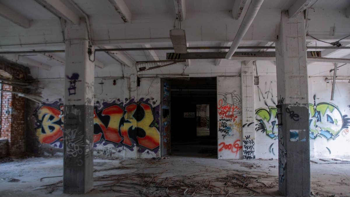 Interior view of an abandoned industrial building featuring colorful graffiti on walls and empty space.