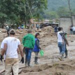 People navigate a muddy terrain in Mocoa, Colombia, post-flood recovery efforts.