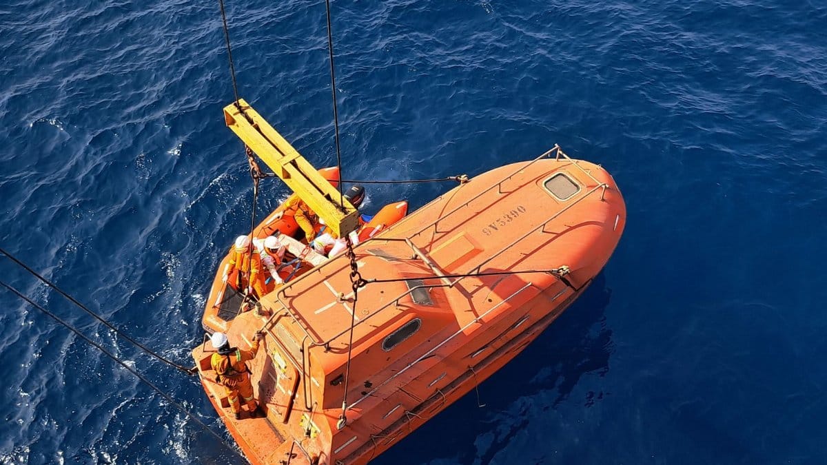 An aerial view of an orange lifeboat being lowered onto the ocean surface, safe and secure.