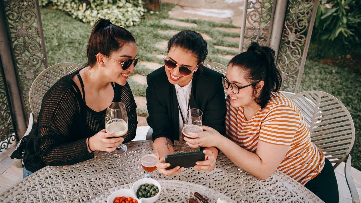 Three women sitting outdoors, sharing moments over drinks. Captured in a garden setting.
