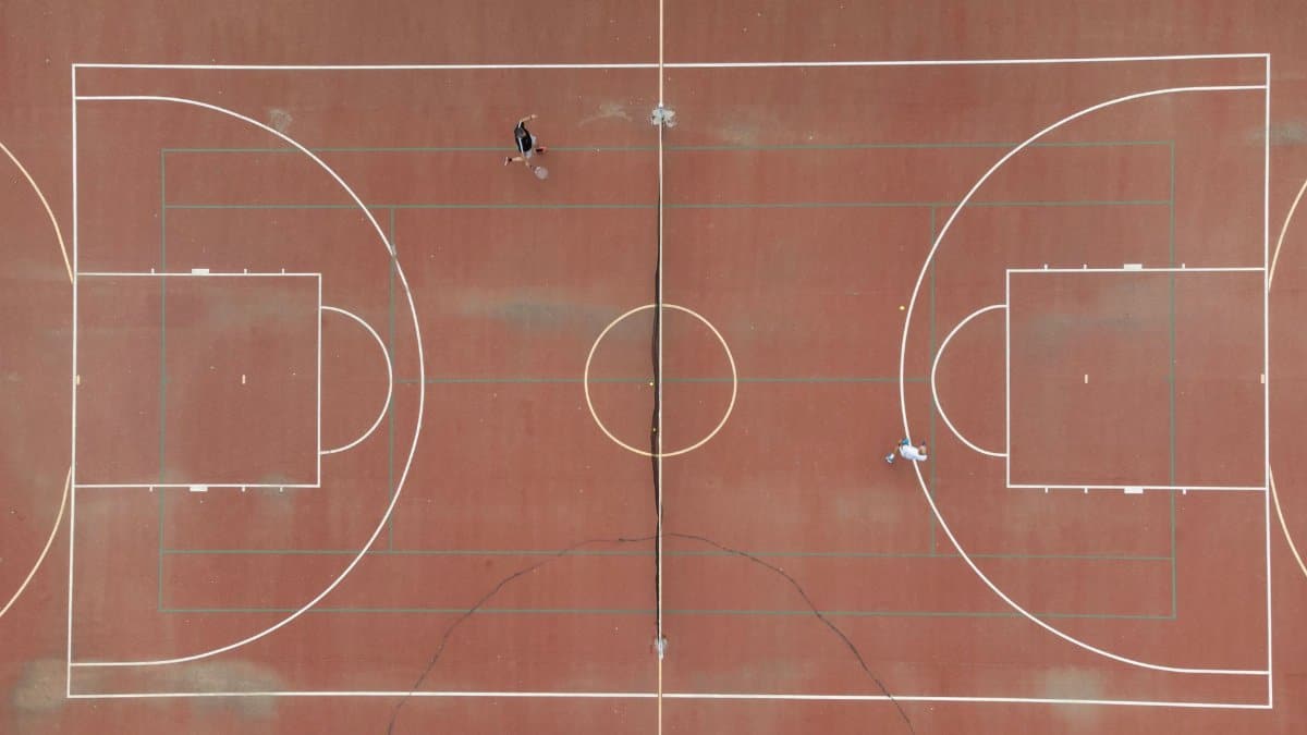 A drone shot of a tennis court with two players engaged in a game, taken from above.