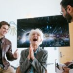 A happy elderly woman laughing while trying virtual reality with friends indoors.