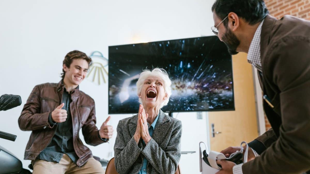 A happy elderly woman laughing while trying virtual reality with friends indoors.
