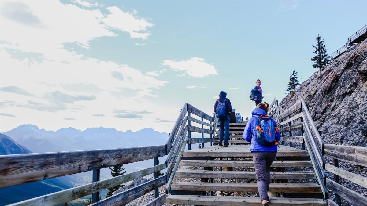 Three hikers climb wooden stairs overlooking a stunning mountain landscape.