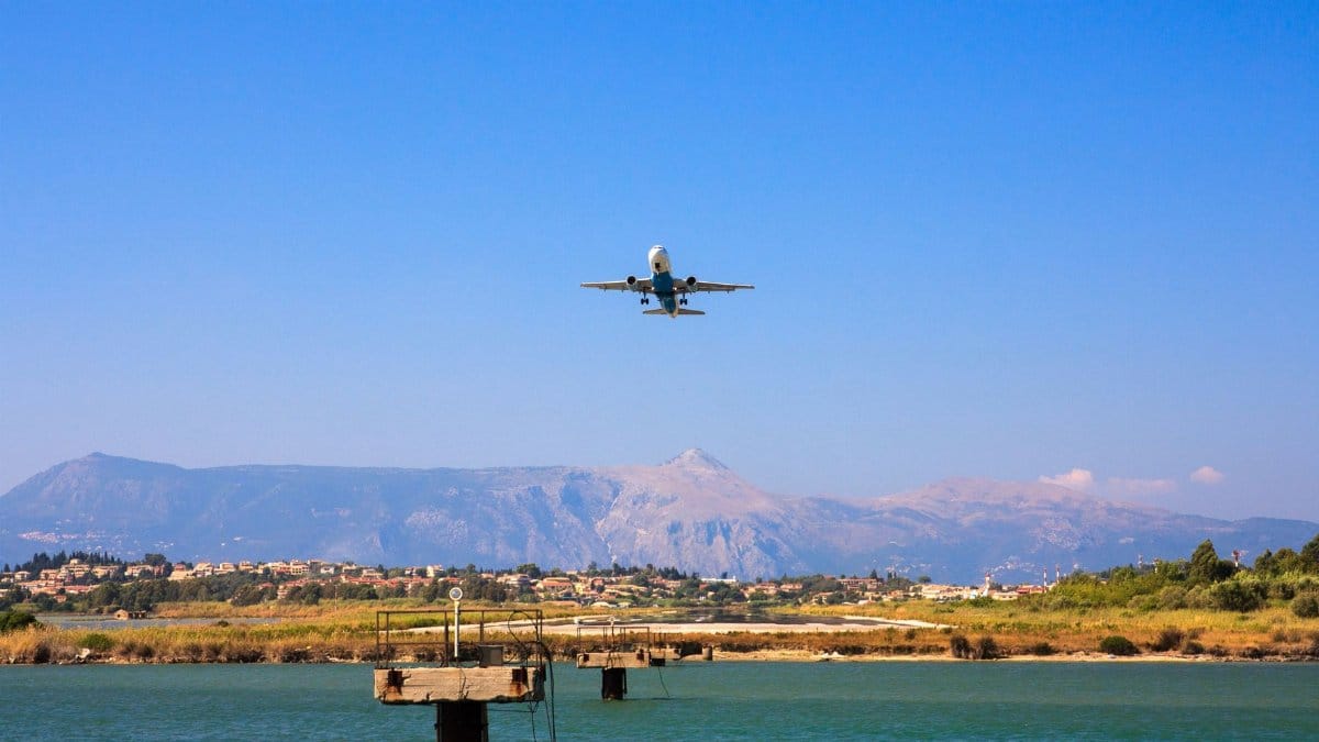 A plane flying over Corfu, Greece with mountains and water below, capturing a vibrant day scene.