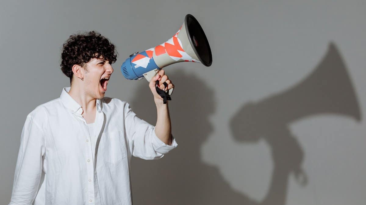 Young adult with curly hair energetically shouting through a colorful megaphone.