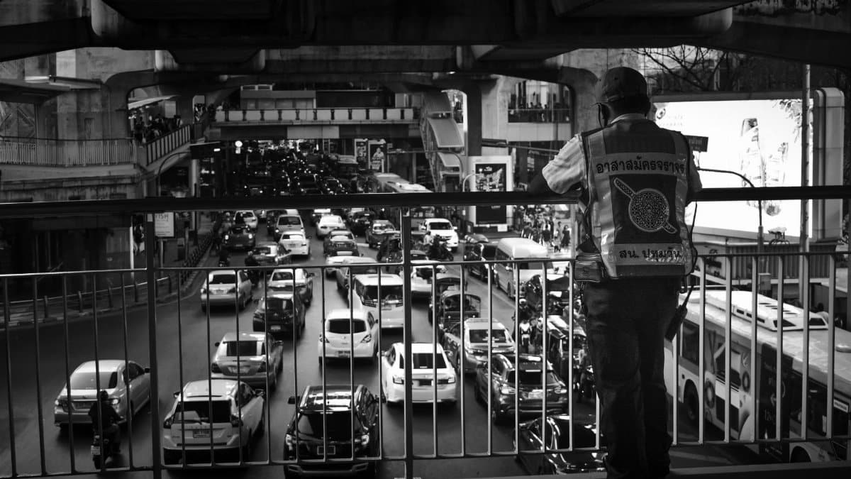 Monochrome view of bustling traffic from a Bangkok overpass, with a person observing the city flow.