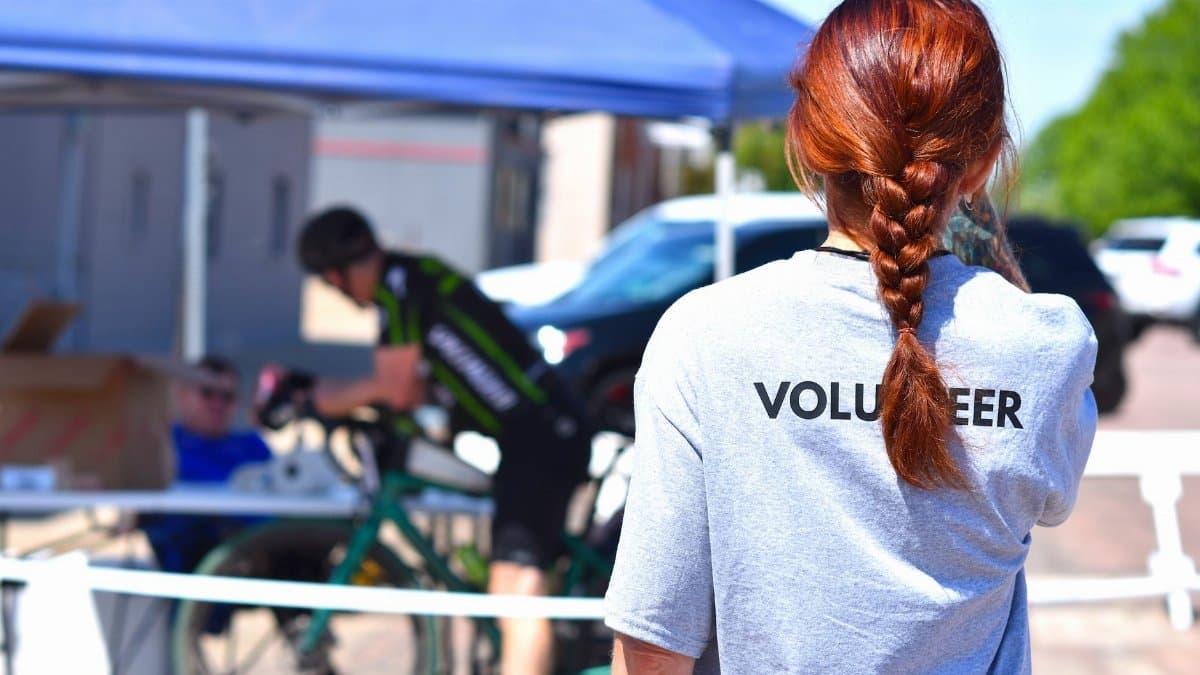 A volunteer oversees a charity bike event under a blue tent on a sunny day.