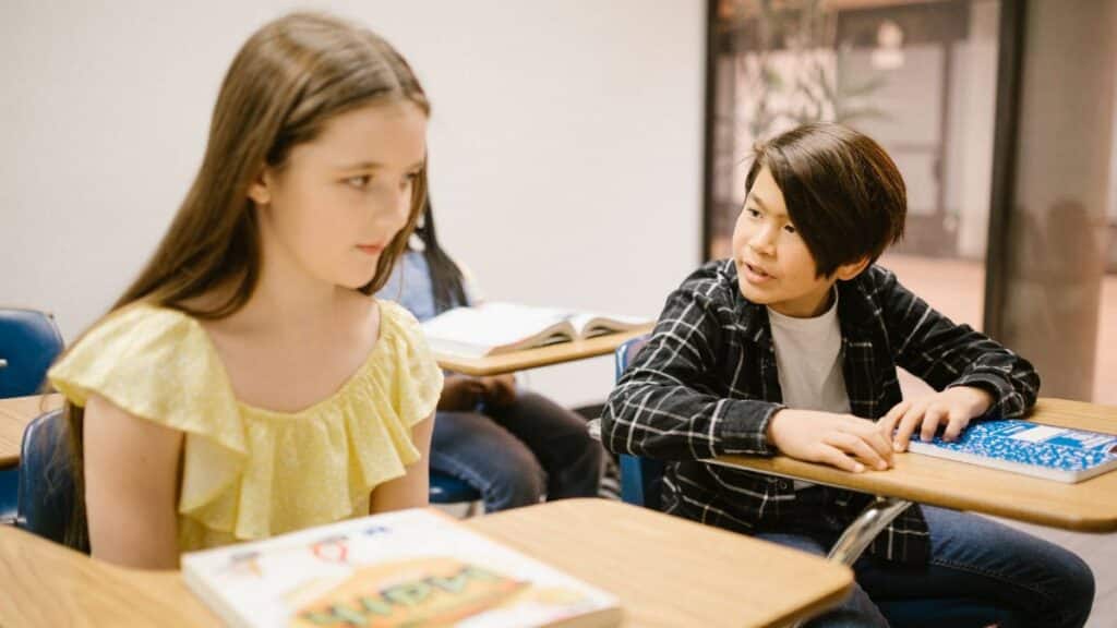 Two students in a classroom interacting with each other during a lesson.
