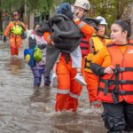Rescue workers in orange gear helping people during a flood, showcasing bravery and teamwork.