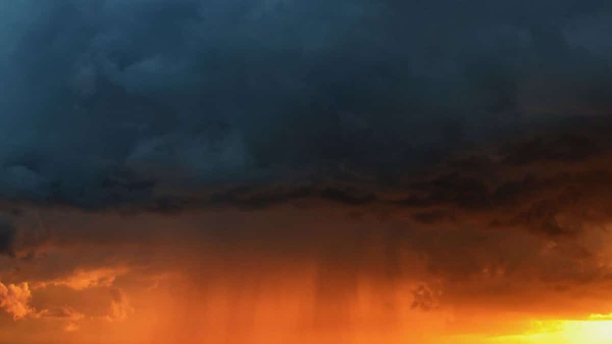 Vivid storm clouds with rain illuminated by a striking sunset sky.