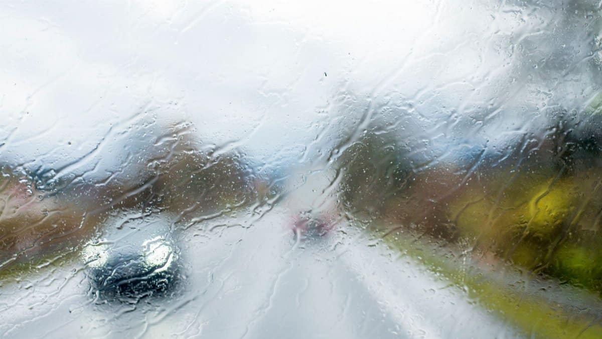 A car seen through a rain-soaked windshield, depicting a rainy day drive.