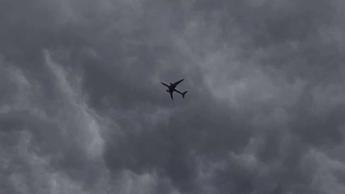 A silhouette of an airplane flying amidst dark storm clouds, showcasing aviation and weather phenomena.