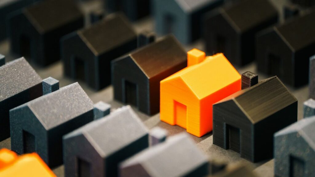 Striking orange model house stands out among black miniature houses, symbolizing real estate choices.