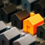 Striking orange model house stands out among black miniature houses, symbolizing real estate choices.
