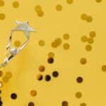 A silver trophy with a star design on a vibrant yellow background adorned with confetti.