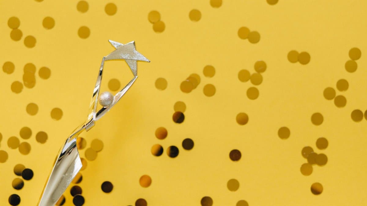 A silver trophy with a star design on a vibrant yellow background adorned with confetti.