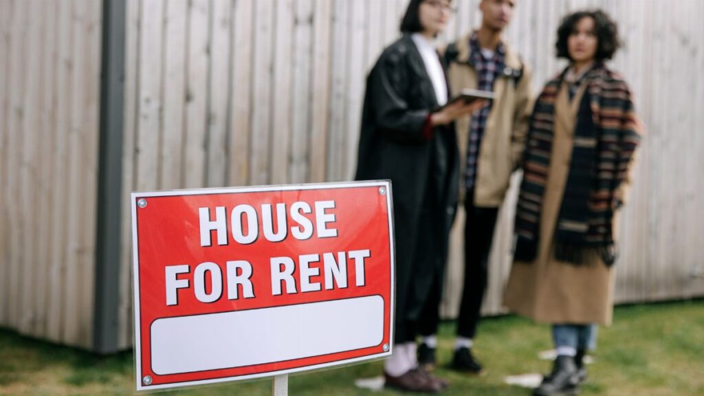Three adults examining a house for rent sign outdoors, depicting diverse and inclusive interest in rental properties.
