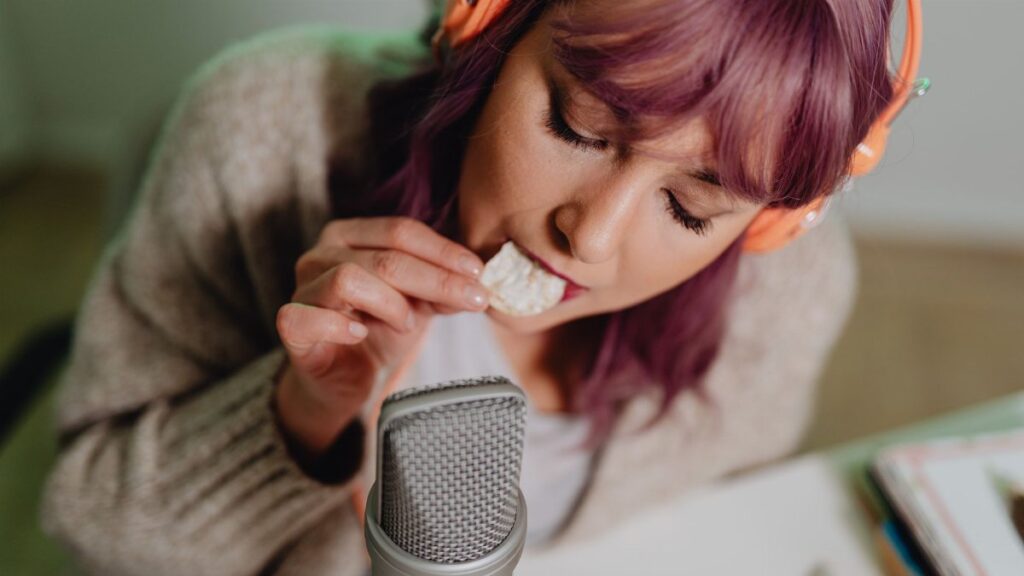Close-up of a woman recording ASMR eating sounds with headphones and microphone.