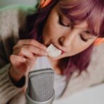 Close-up of a woman recording ASMR eating sounds with headphones and microphone.