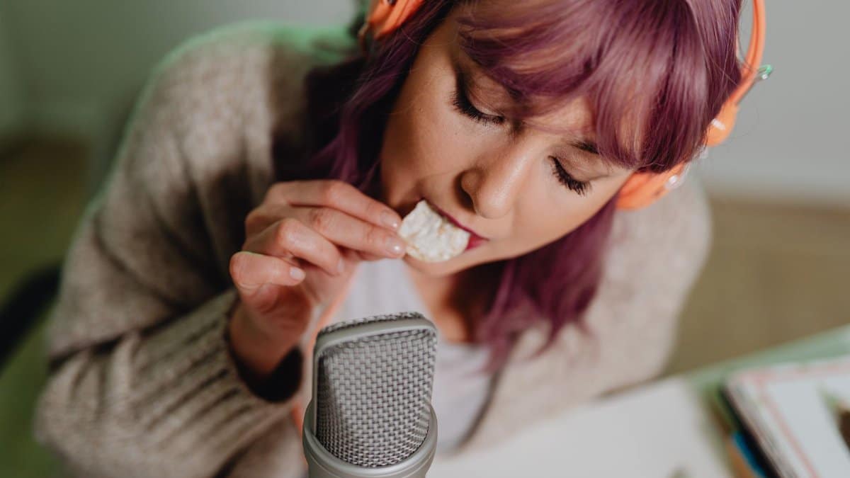 Close-up of a woman recording ASMR eating sounds with headphones and microphone.