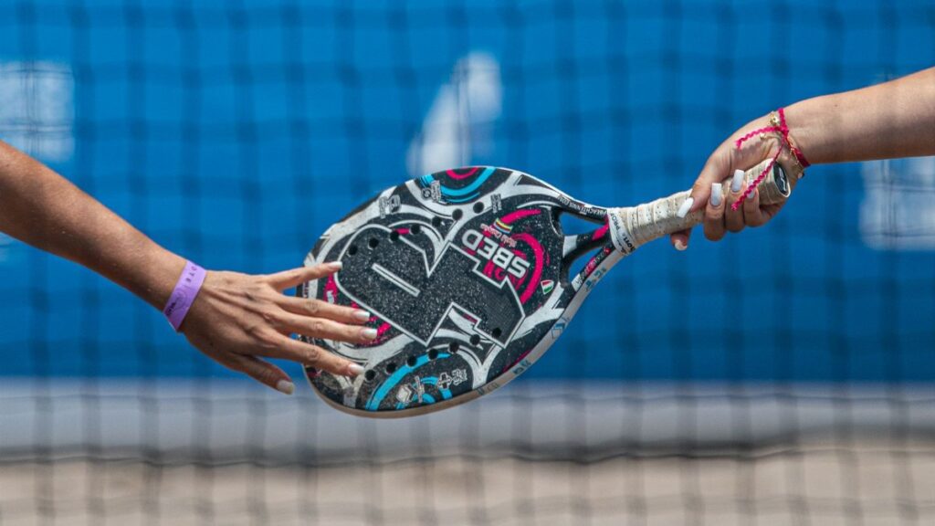 Close-up of two players exchanging a padel racket on an outdoor court.
