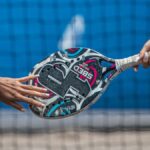 Close-up of two players exchanging a padel racket on an outdoor court.
