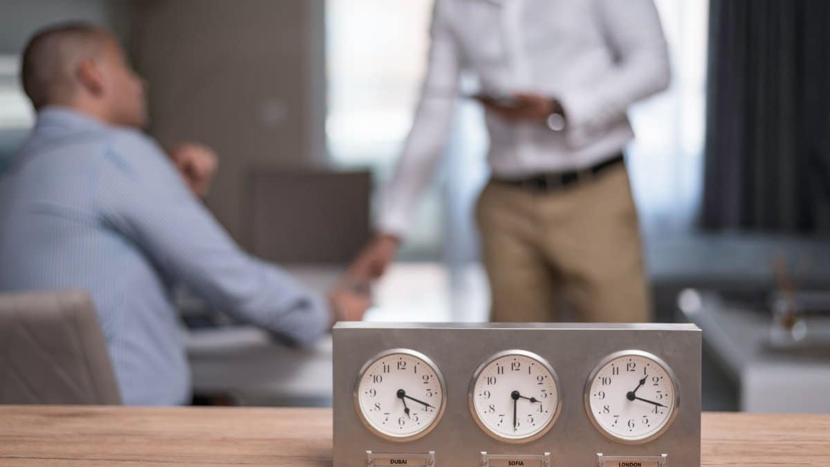 Two businessmen in an office with clocks showing different time zones, symbolizing global business.