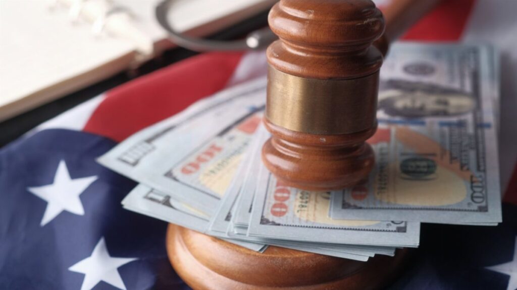 Close-up of a judge's gavel resting on US dollar bills and an American flag, symbolizing justice and finance.