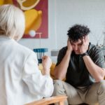 A therapist consults a distressed man in a cozy setting.