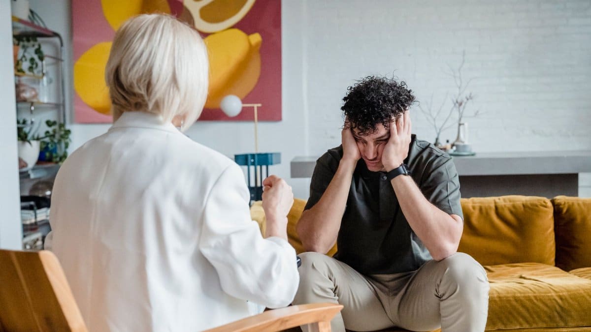 A therapist consults a distressed man in a cozy setting.