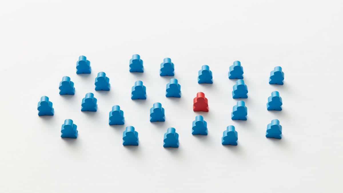 A red meeple stands out in a pattern of blue figures, symbolizing individuality.