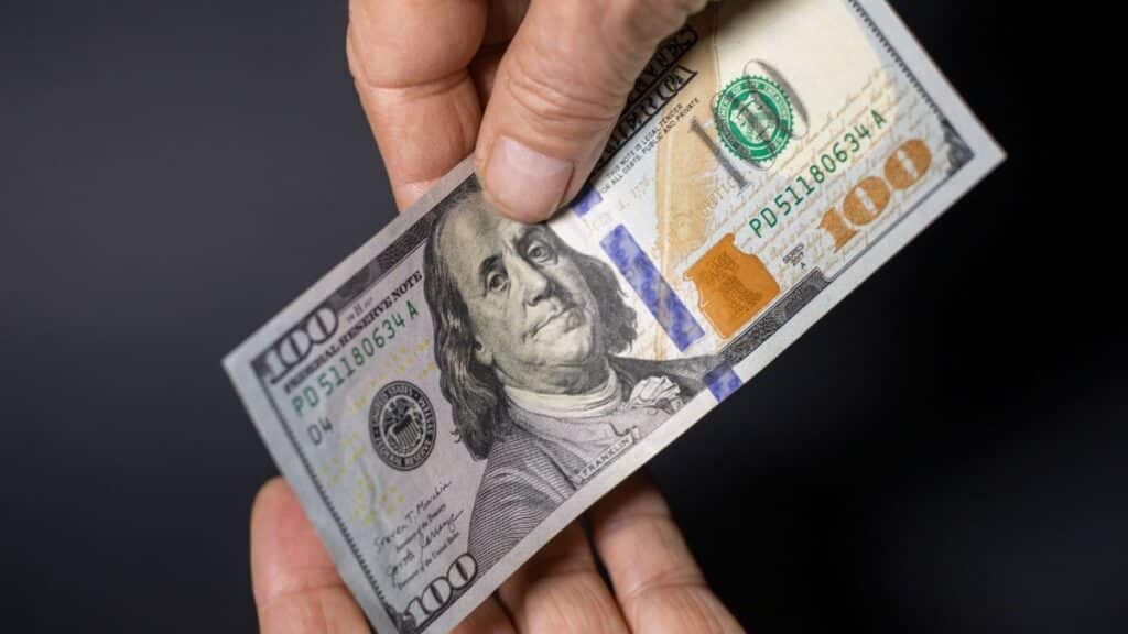 Detailed image of hands exchanging a crisp one hundred dollar bill, symbolizing financial transactions.
