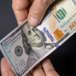 Detailed image of hands exchanging a crisp one hundred dollar bill, symbolizing financial transactions.