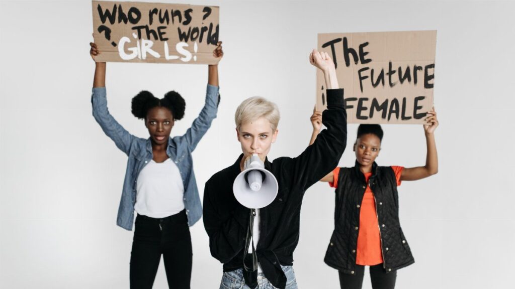 Diverse women protesting with placards and megaphone in a studio setting.
