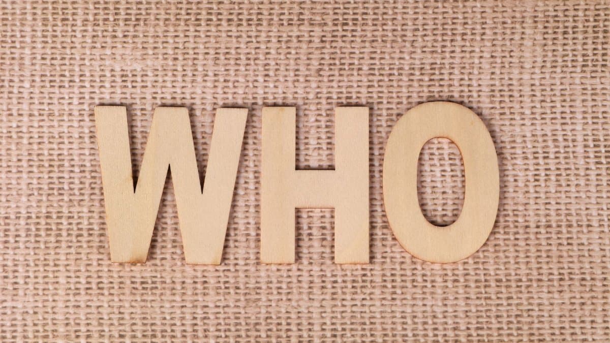 Wooden letters spelling 'WHO' on a textured burlap fabric, emphasizing identity or inquiry.