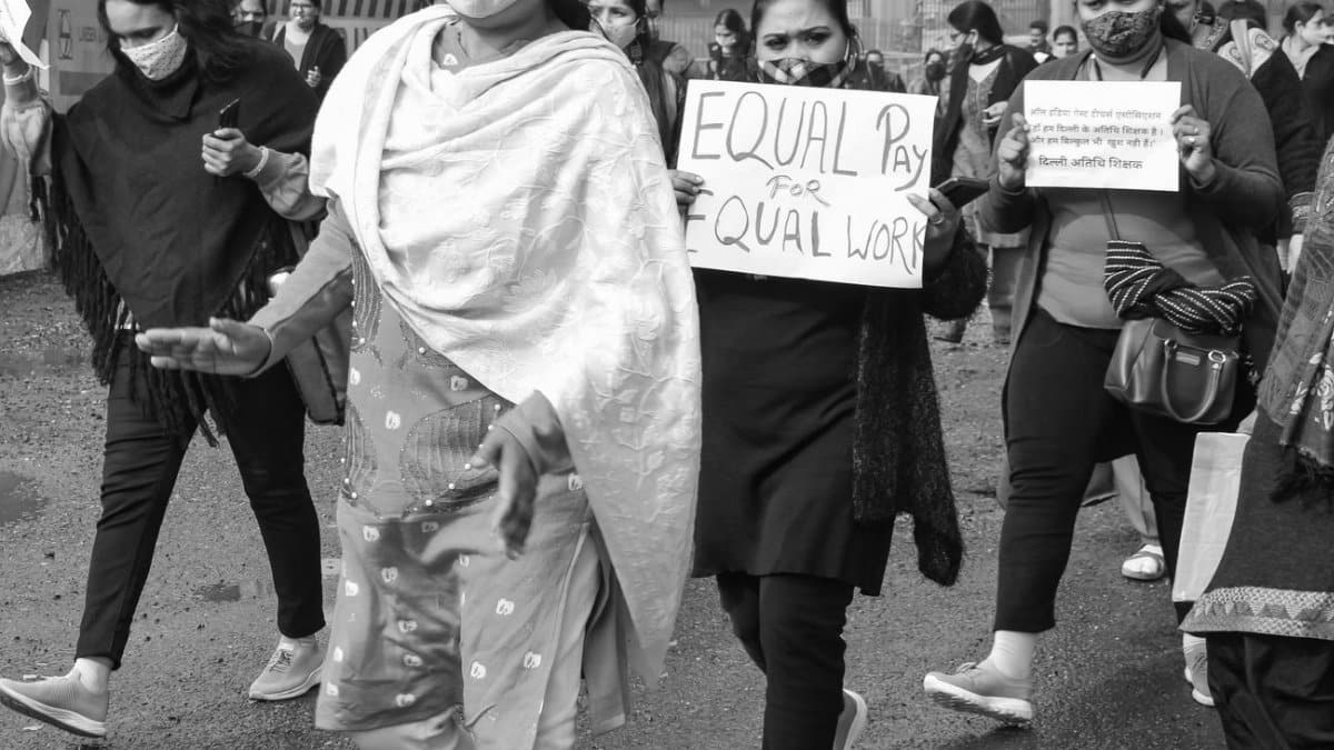 A black and white image of a women's rally advocating for equal pay, with participants wearing face masks and holding placards.