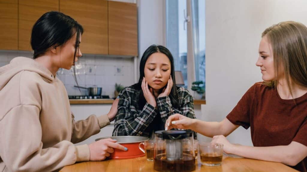 Three women gathered at a kitchen table, offering comfort and support to a sad friend.