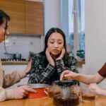 Three women gathered at a kitchen table, offering comfort and support to a sad friend.