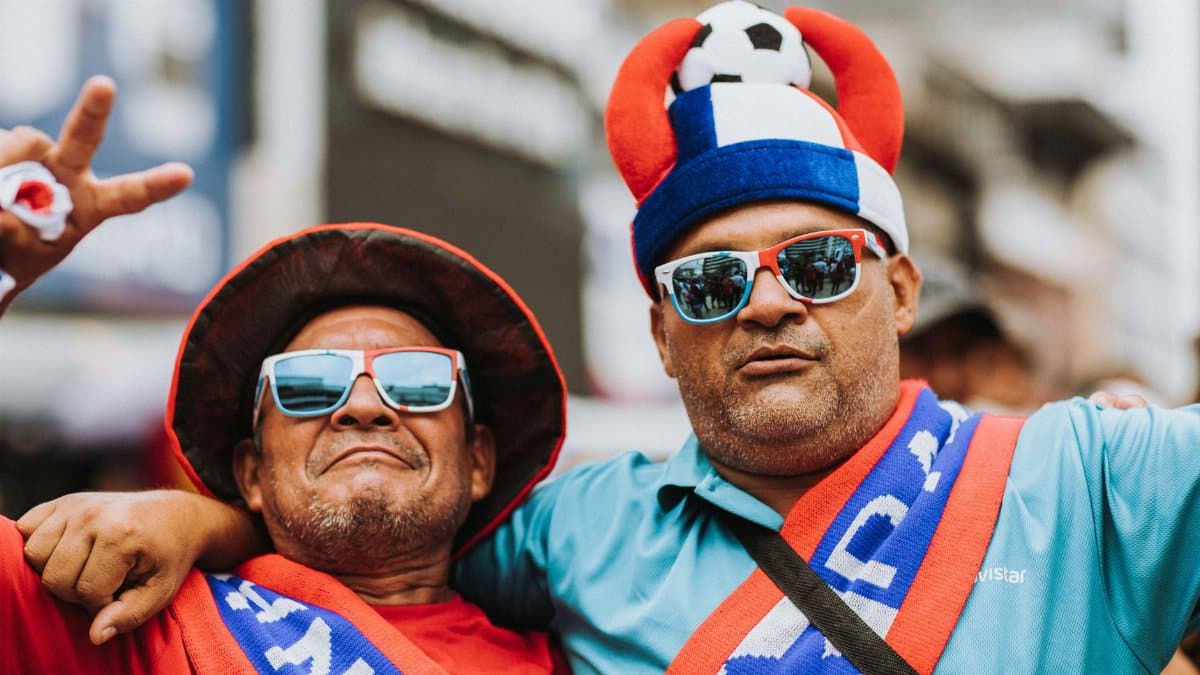 Two joyful soccer fans in vibrant attire show their excitement outdoors.