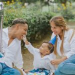 A joyful family celebrating their child's first birthday outdoors with cake and balloons.
